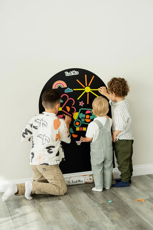 Three children playing with Tix&Mix Rings and Blocks set on a black magnetic wall decal.