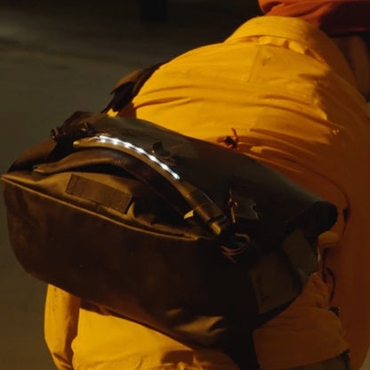 A person with a backpack is using a light for visibility at night.
