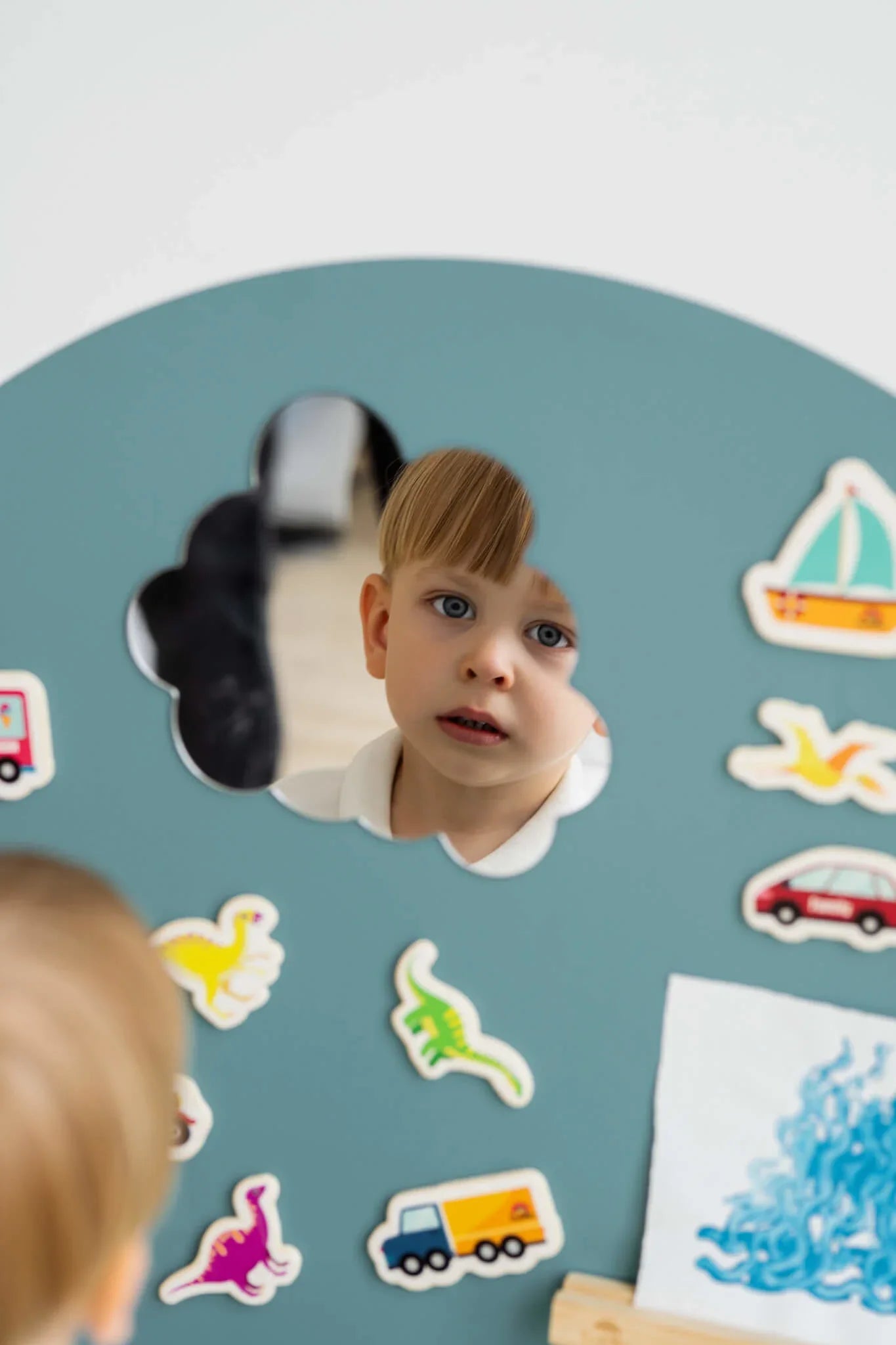A male child looking at his reflection on a Tix&Mix magnetic mirror on a cyan wall decal.