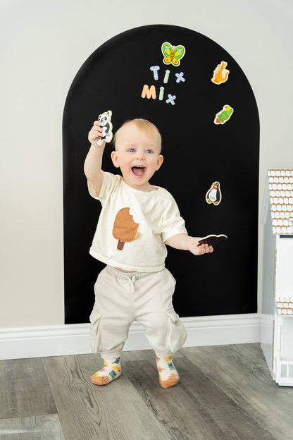 A toddler happily playing with TixMix magnetic toys on a black magnetic wall decal.
