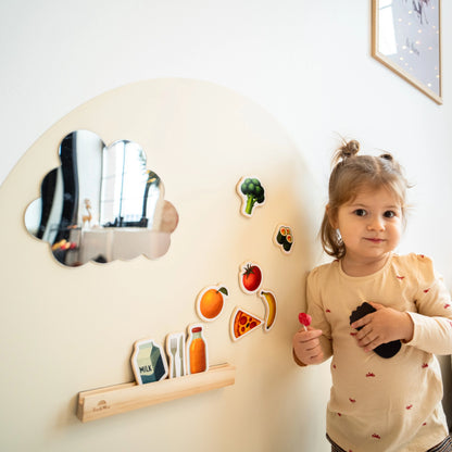 A female toddler looking at the camera while playing with Tix&Mix magnetic foods games set on a white wall decal.