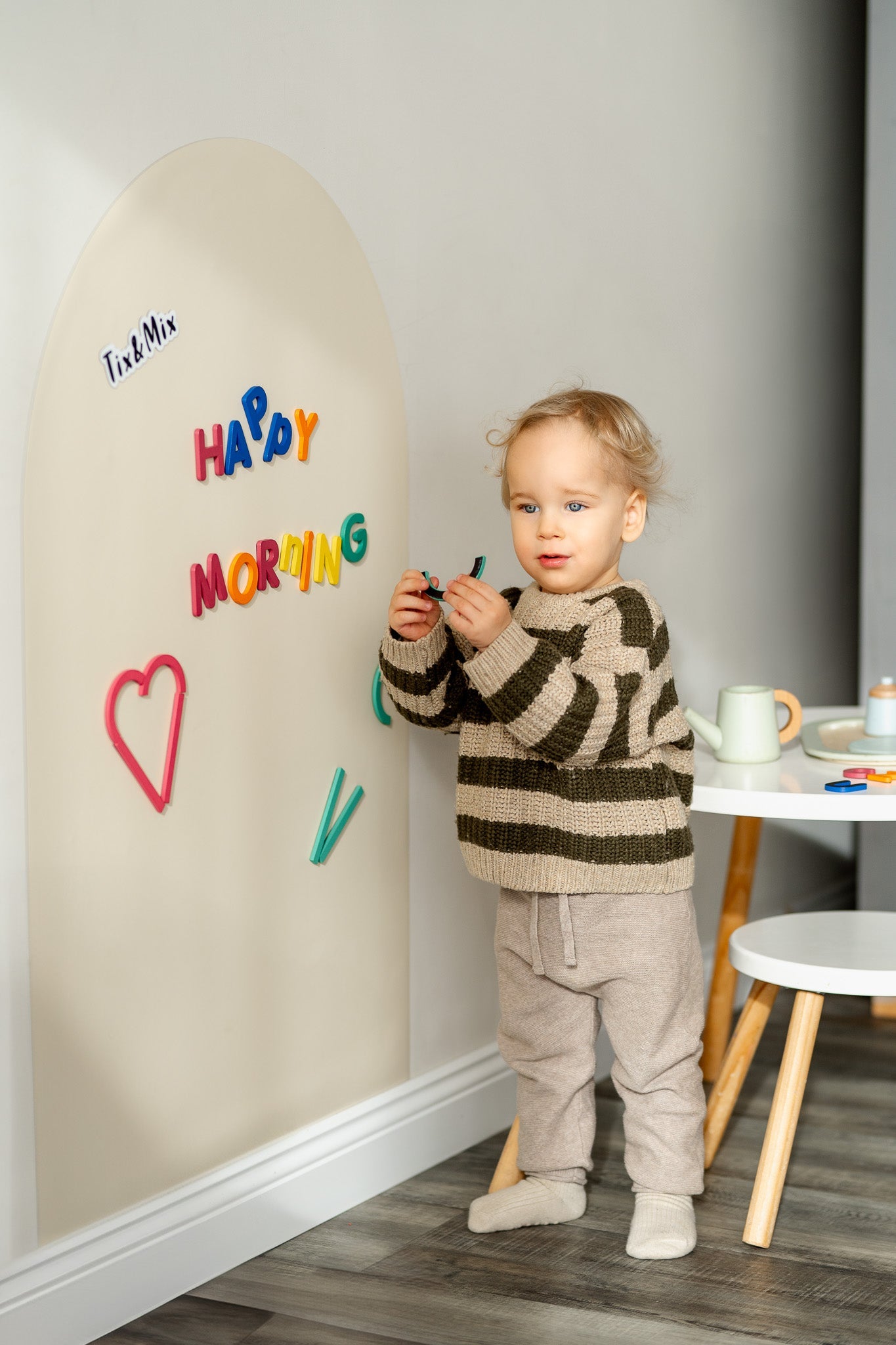 A toddler playing with Tix&Mix Rings and Blocks play set on a magnetic wall decal in White Pudding color.