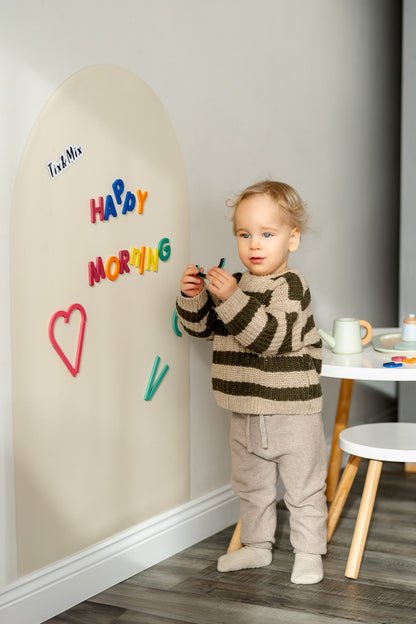 A toddler playing with Tix&Mix Rings and Blocks play set on a magnetic wall decal in White Pudding color.