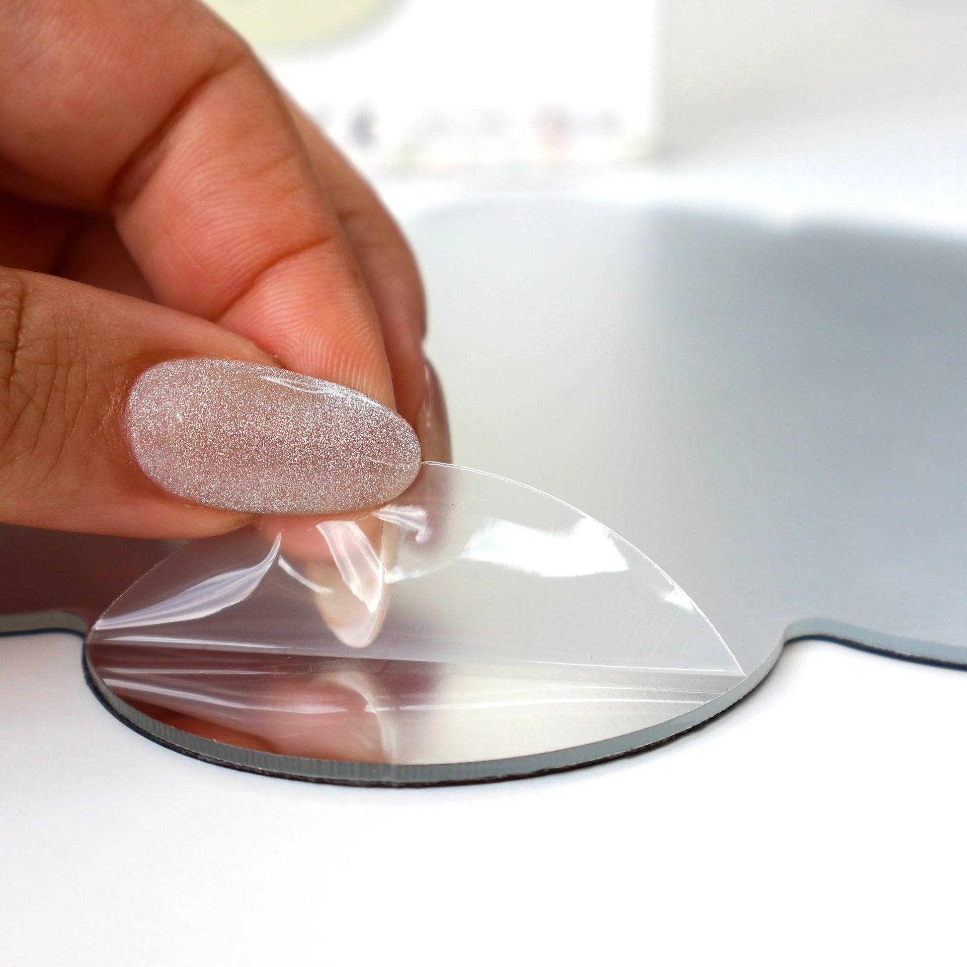 A hand removing the white outer sticker from the Tix&Mix magnetic mirror.