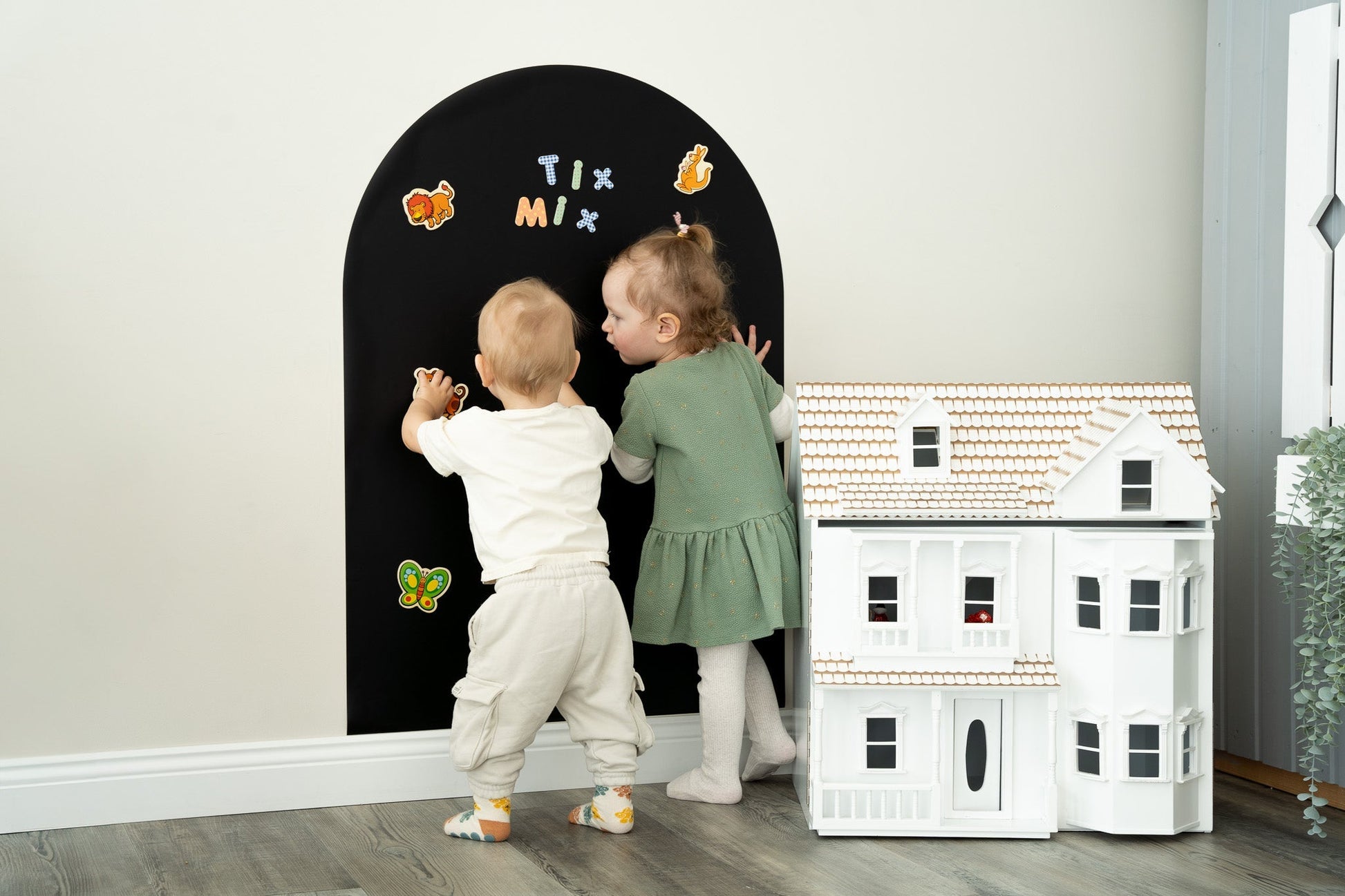 Two toddlers playing with Tix&Mix magnetic toys on a black magnetic wall decal.
