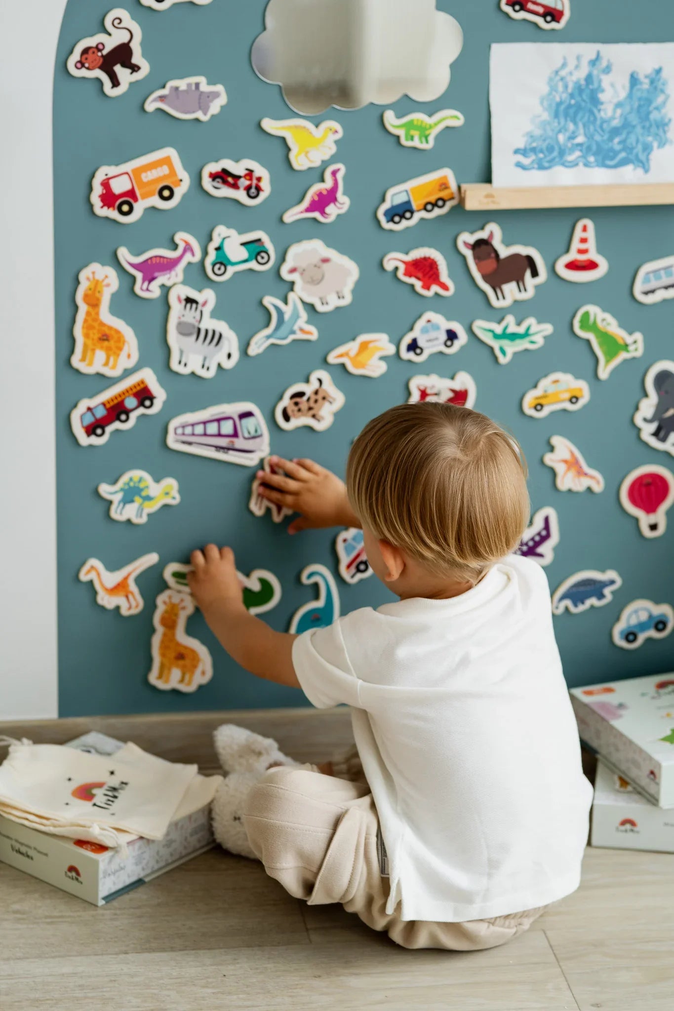 A male kid playing with Tix&Mix magnetic animals and vehicles toys on a cyan wave wall decal.